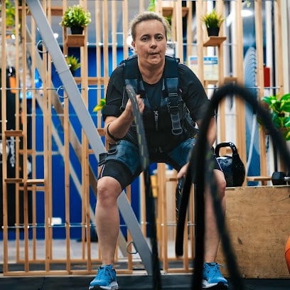 Femme s'exerçant avec des battle ropes et une veste EMS pour un entraînement de fitness intense.