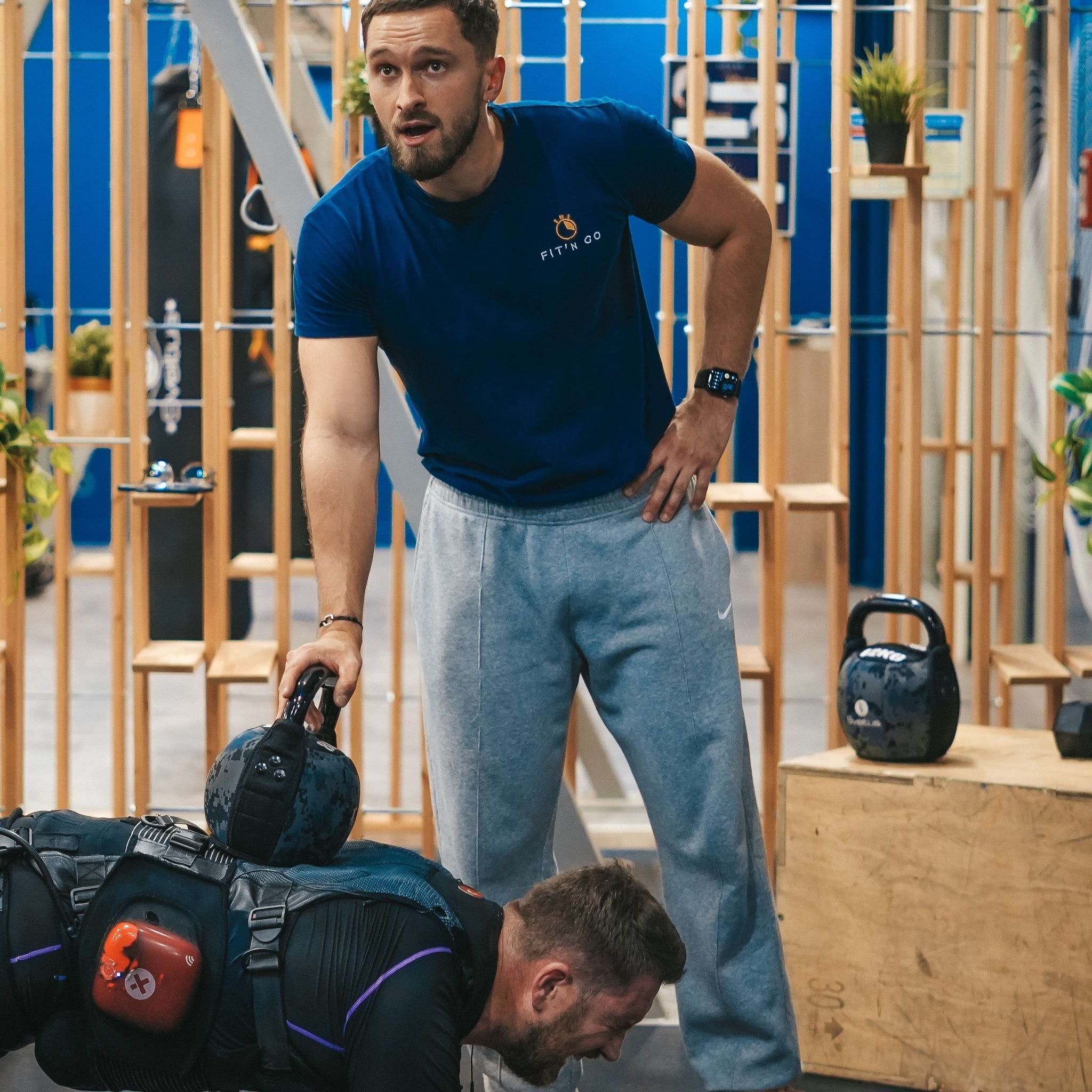 Coach Fit'n Go supervisant un exercice intense avec kettlebell et gilet lesté en salle de sport.