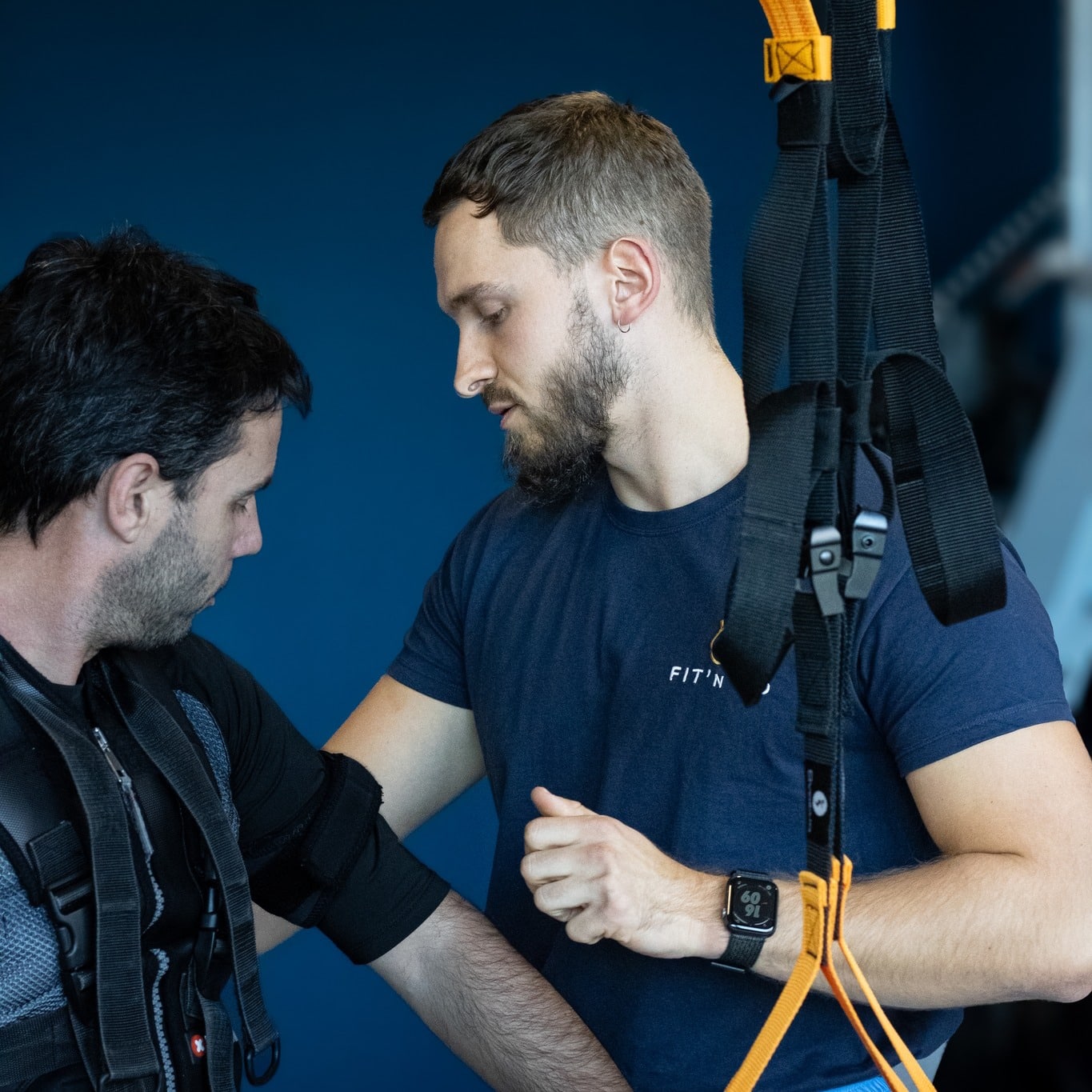 Coach Fit'n ajustant une tenue d'électrostimulation EMS sur un sportif pour une séance de fitness personnalisée.